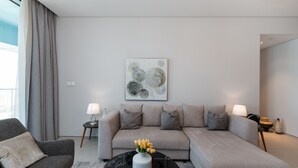 A modern living room with a grey sofa, a black coffee table with a vase of flowers, and a minimalist wall art piece. - Address JBR 2BR Steps to Beach Bluewaters (Dubai)