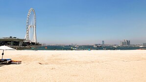 A beach with a Ferris wheel in the background and boats on the water. - Address JBR 2BR Steps to Beach Bluewaters (Dubai)