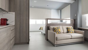 A modern living room with a sofa, a coffee machine, and a bed in the background. - Dobo Madrid Las Torres (Madrid)
