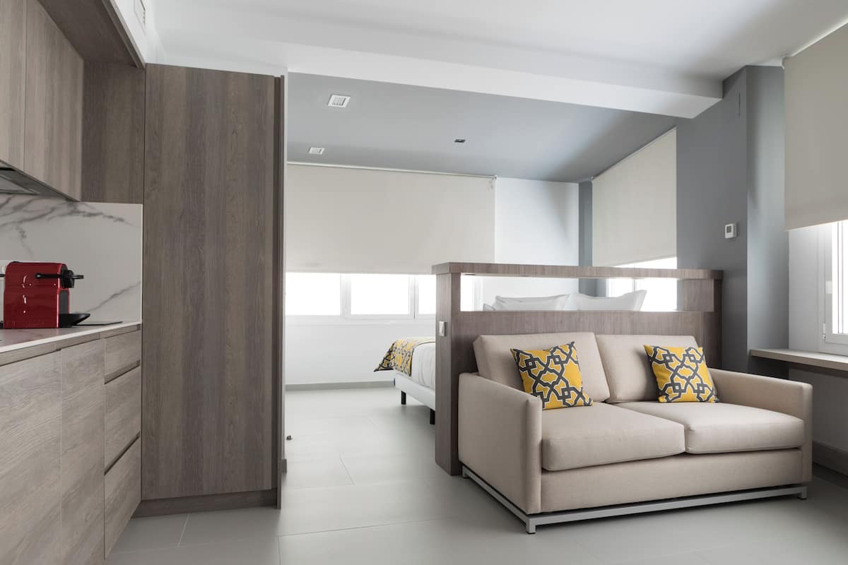 A modern living room with a sofa, a coffee machine, and a bed in the background.