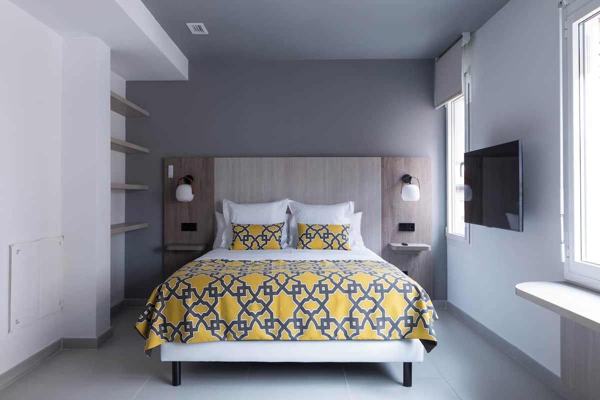 A modern bedroom with a bed, bedside tables, a mounted TV, and built-in shelves.