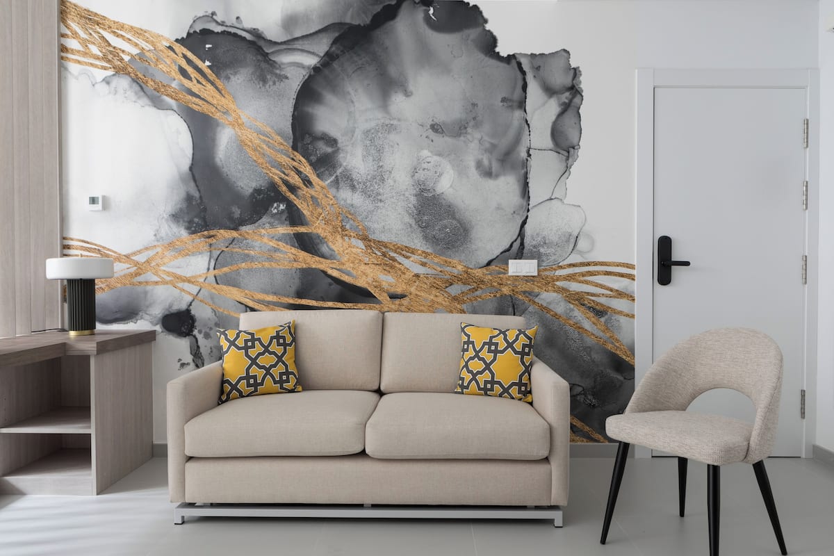 A modern living room with a beige sofa, two patterned cushions, a side table, and a large abstract wall mural.