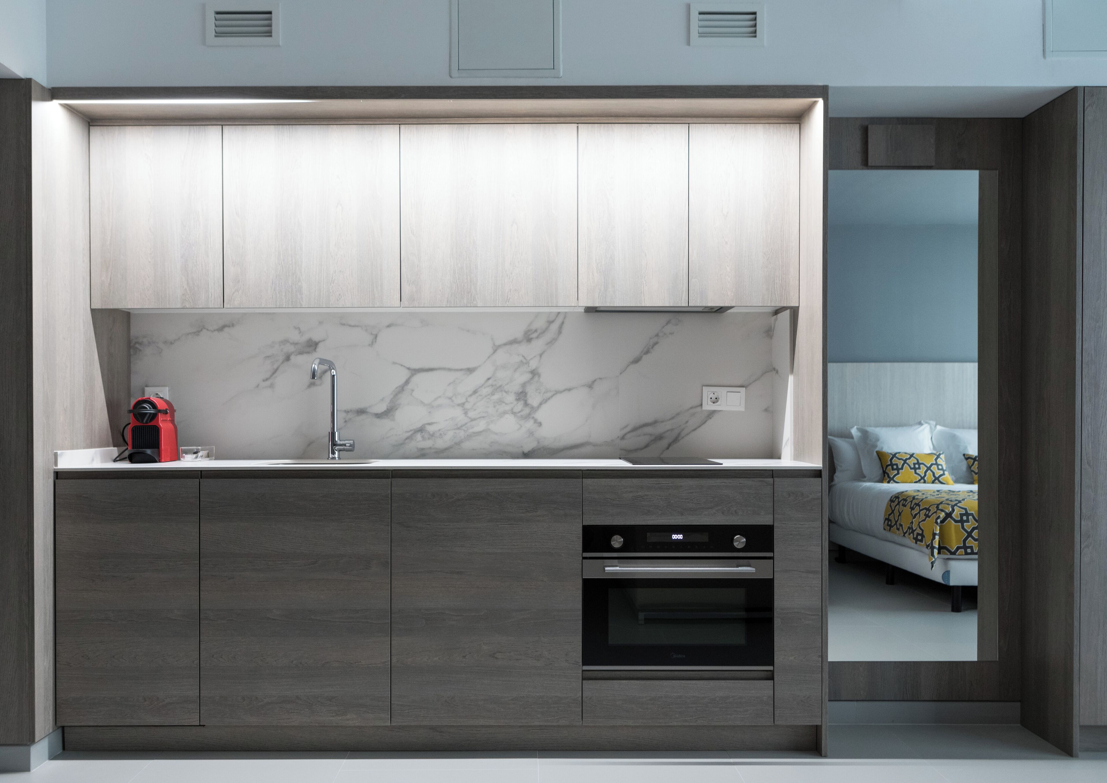 A modern kitchen with a marble backsplash, built-in oven, and grey cabinetry.
