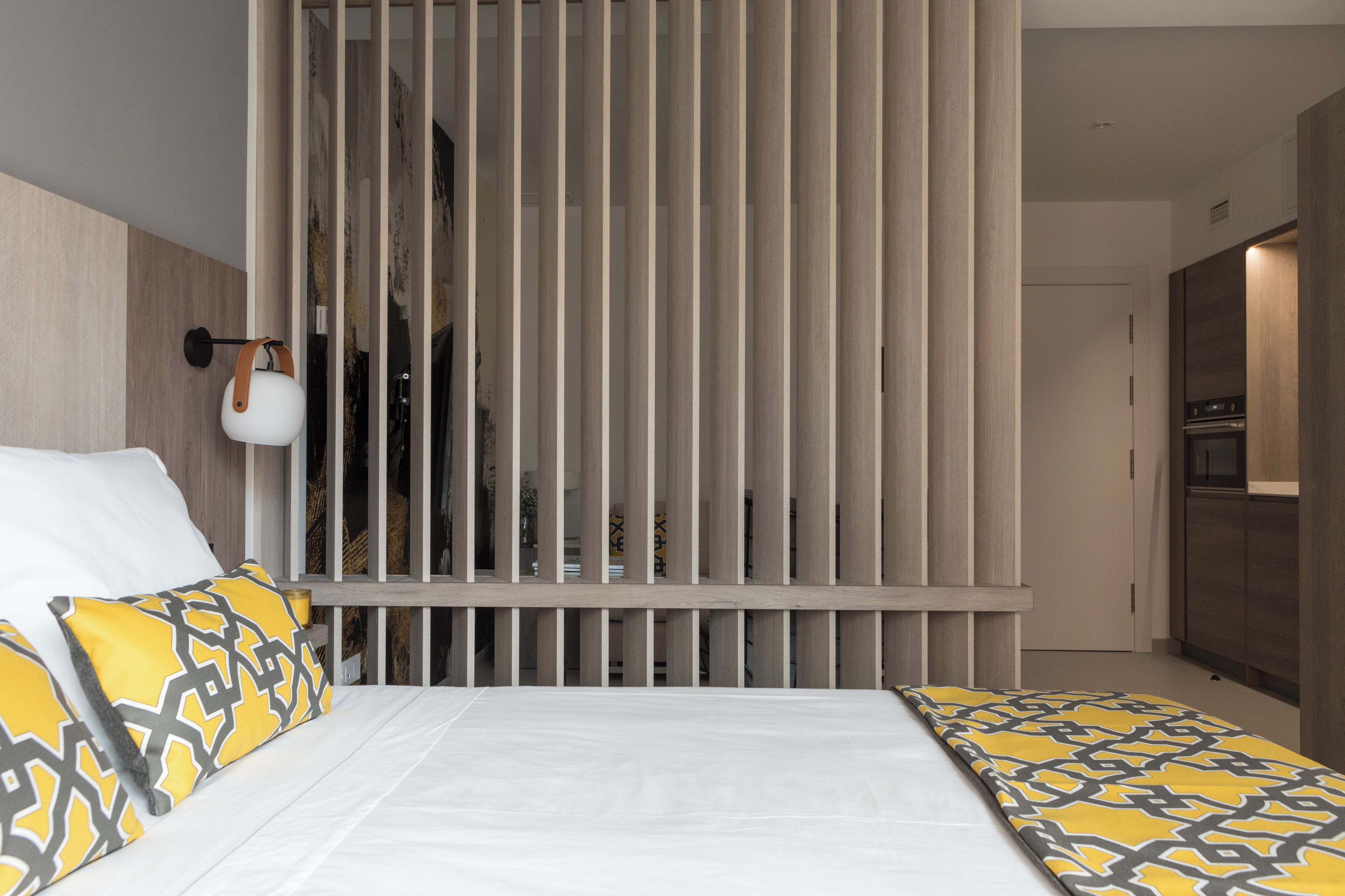 Een moderne hotelkamer met een bed, een houten scheidingswand en een kitchenette.