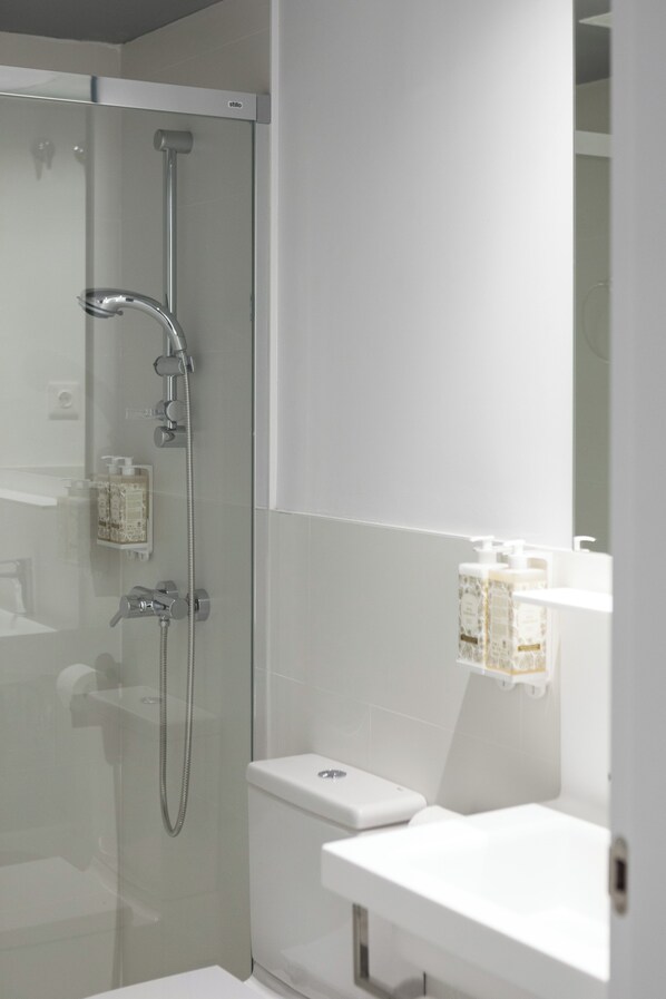 A modern bathroom with a glass-enclosed shower, a white toilet, and a white sink with a mirror above it. - Dobo Madrid Las Torres (Madrid)