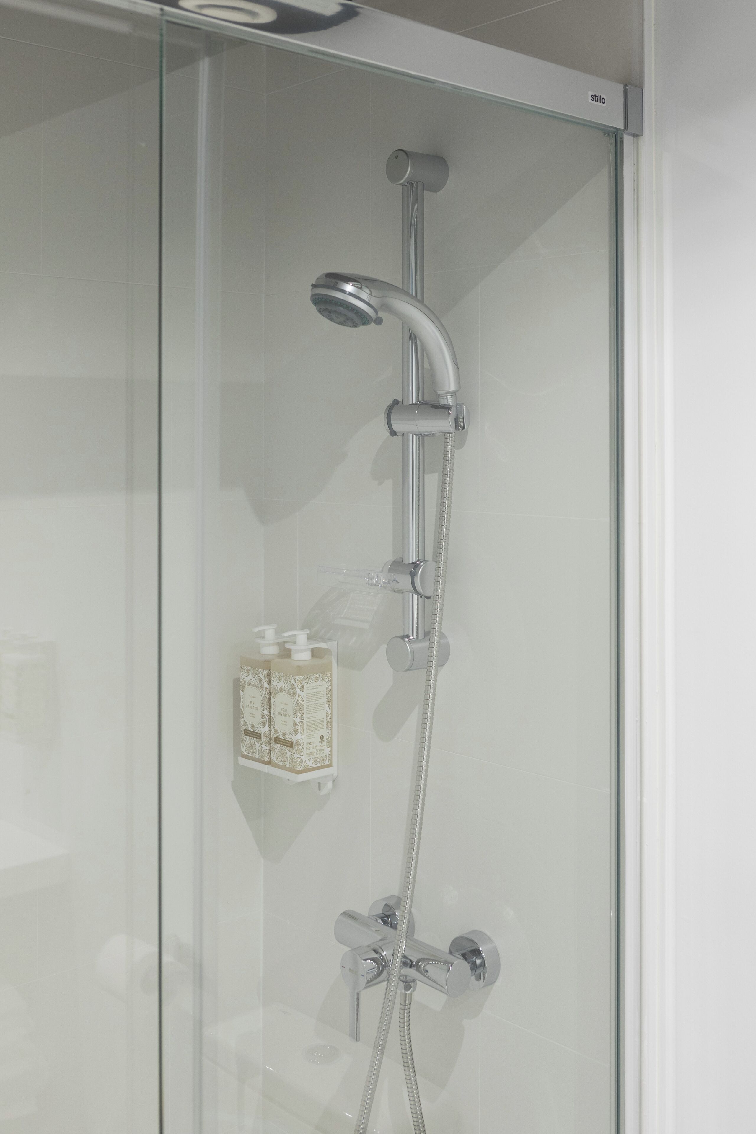 Ducha con cerramiento de vidrio, cabezal de ducha de mano y llave de pared.