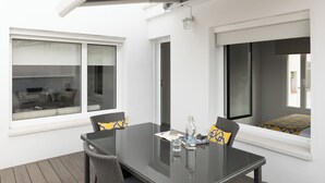 A modern outdoor dining area with a glass table, wicker chairs, and a view of the interior. - Dobo Madrid Las Torres (Madrid)