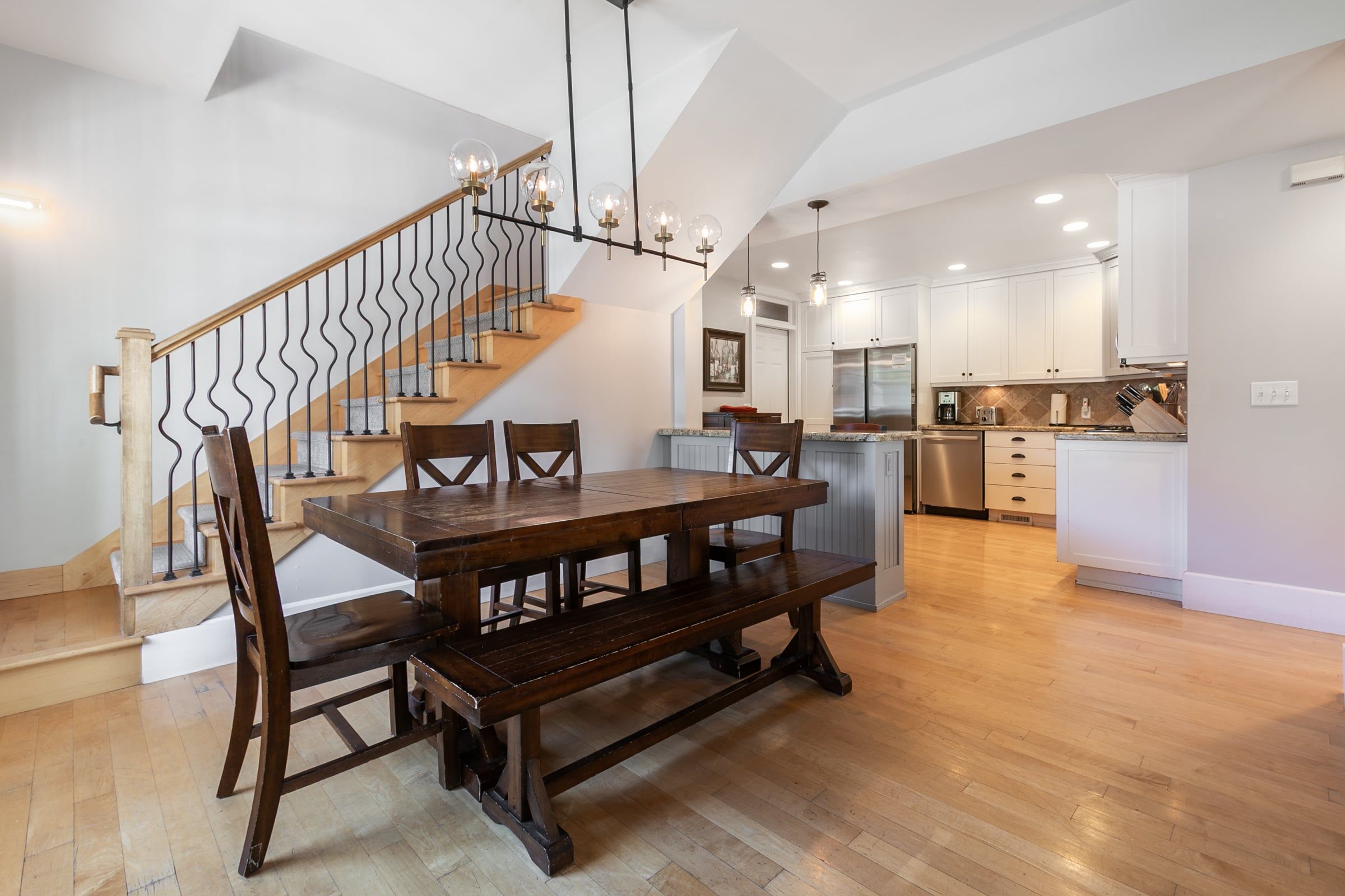 A spacious kitchen with white cabinets, a stainless steel refrigerator, and a wooden dining table with chairs.