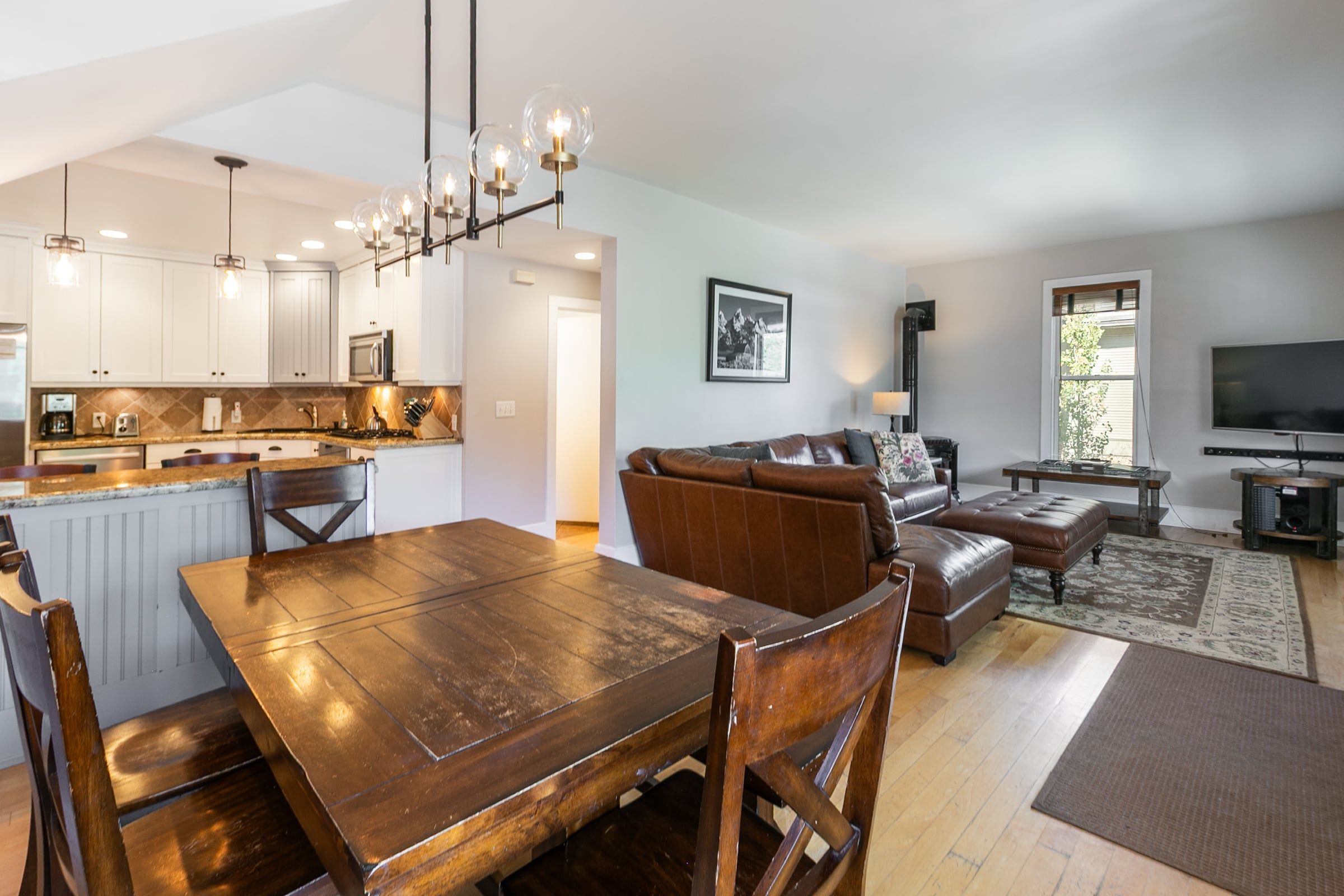 A spacious living area with a dining table, leather sofa, and a flat-screen TV.