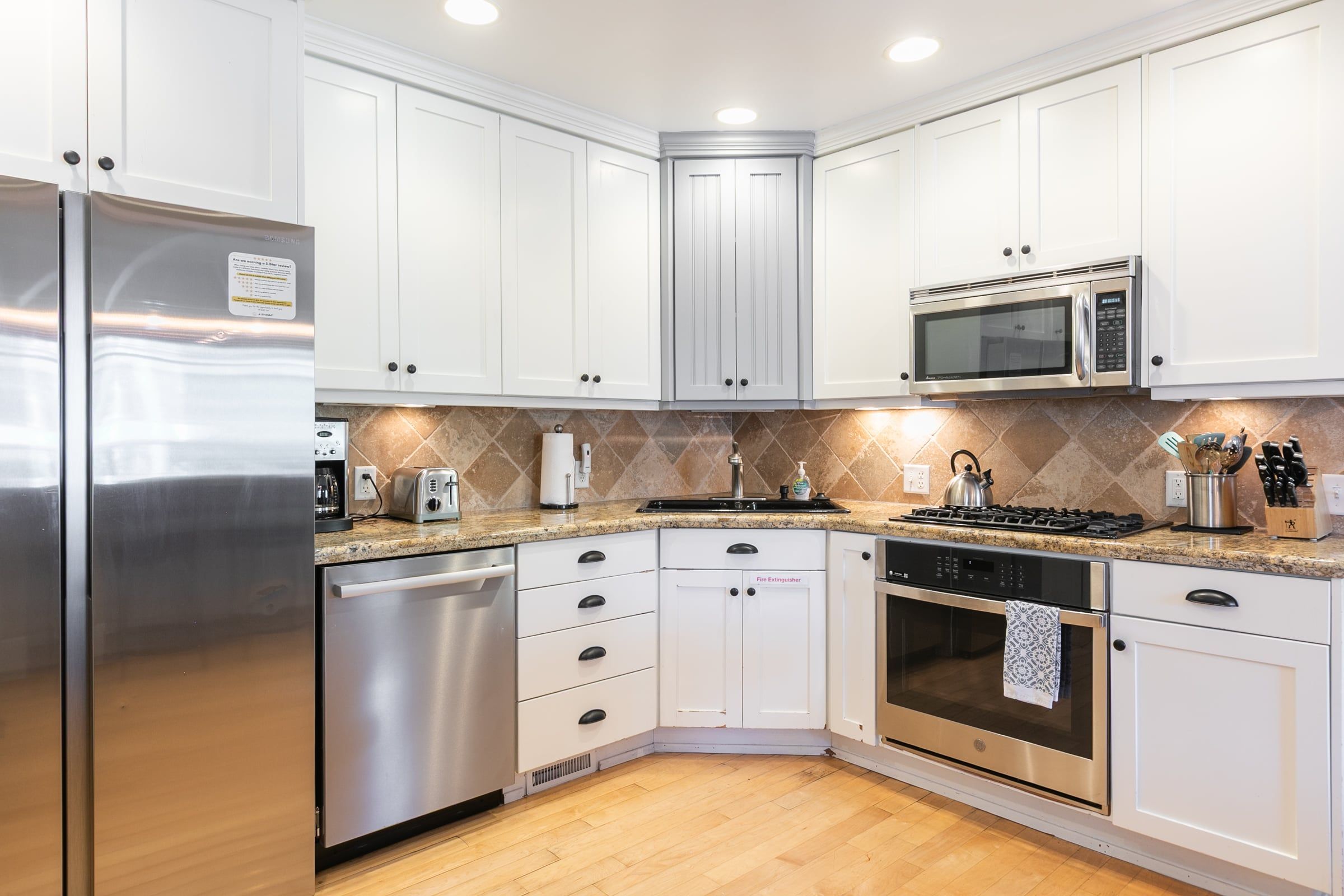 A modern kitchen with white cabinets, stainless steel appliances, a granite countertop, and a tiled backsplash.