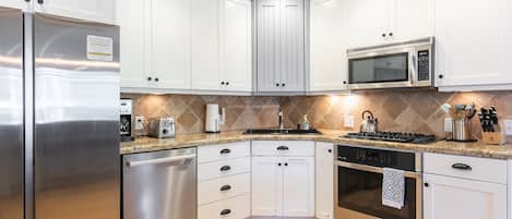 A modern kitchen with white cabinets, stainless steel appliances, a granite countertop, and a tiled backsplash.