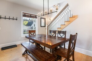 A dining area with a wooden table and benches, a staircase with a metal railing, and a window with blinds.