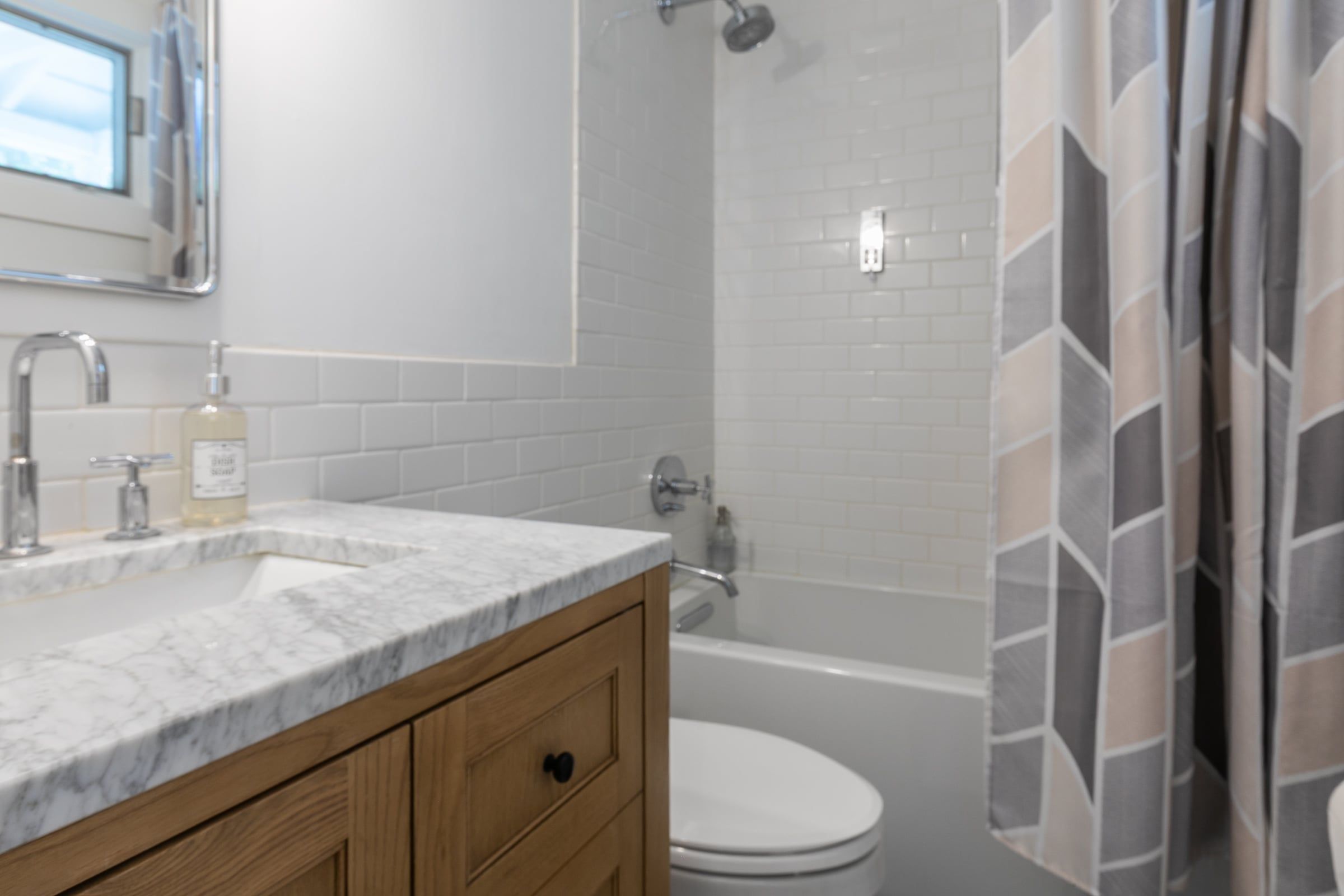 A bathroom with a marble sink, wooden cabinet, white toilet, and a shower with a geometric-patterned curtain.