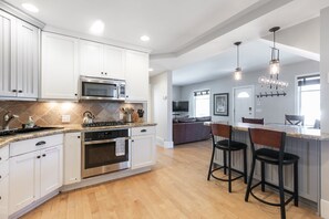 A modern kitchen with white cabinets, stainless steel appliances, and a central island with bar stools. - Historic Charm in the Heart of Old Town Park City- Walk to Ski, Private Hot Tub (Park City)
