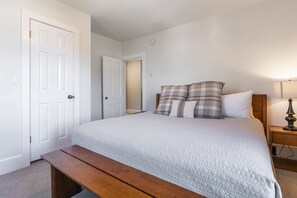 A bedroom with a bed, a bench, a nightstand, and a door.