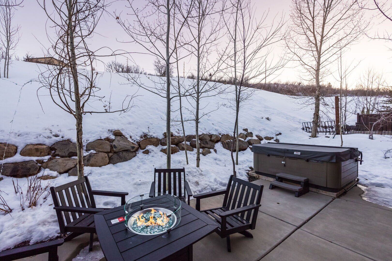 An outdoor patio with a fire pit table, four chairs, and a hot tub.