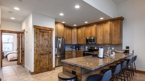 A modern kitchen with wooden cabinets, stainless steel appliances, a granite countertop, and bar stools. - Summer by the Lake! Beautiful Swimming Pool, Patio Hot Tub Firetable BBQ Nature Trails Hiking Biking (Kamas)
