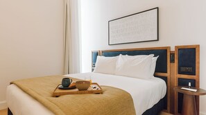 A hotel room with a bed, a bedside table with a lamp, a tray with breakfast items, and a framed picture on the wall. - Ando Living - Abrantes 50 House - 207 (Lisbon)
