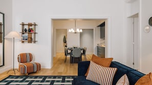 Een moderne woonkamer met een blauwe bank, gestreepte kussens, een kamerbreed tapijt, en een eethoek met een kroonluchter.