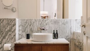 A bathroom with a marble backsplash, a round sink, and two bottles of lotion on the vanity. - Ando Living - Abrantes 50 House - 203 (Lisbon)