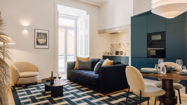 Ein modernes Wohnzimmer mit einem dunkelblauen Sofa, beigen Sessel und einem Couchtisch. Ein Esstisch mit Stühlen und eine Pendelleuchte sind ebenfalls vorhanden.