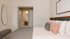 Une chambre d’hôtel comprenant un lit, une chaise, un miroir et une porte donnant sur une salle de bain.