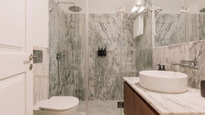 Ein modernes Badezimmer mit einer Marmerdusche, einem weißen Waschbecken und einer Duschkabine aus Glas.