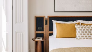 A hotel room with a wooden headboard, white bedding, a mustard-colored pillow, a patterned pillow, and a small round table with a book. - Ando Living - Abrantes 50 House - 301 (Lisbon)