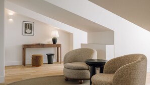 Ein modernes Wohnzimmer mit einem Holzkonsolentisch, zwei Sesseln, einer Stehlampe und einem gerahmten Bild an der Wand.