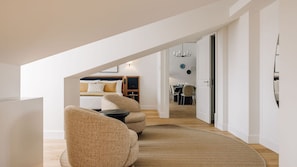A modern loft-style bedroom with a sloped ceiling, a cozy seating area with a round rug, and a dining area visible through an open door. - Ando Living - Abrantes 50 House - 504 (Lisbon)
