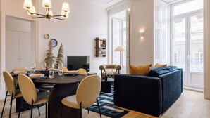 Ein modernes Wohnzimmer mit einem dunkelblauen Sofa, einem Esstisch mit Stühlen und einer Chandelier.