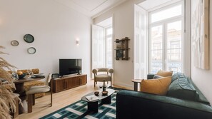 Olohuoneessa on sohva, televisio, puinen kaappi ja ikkunasta avautuu näkymä ulos.
