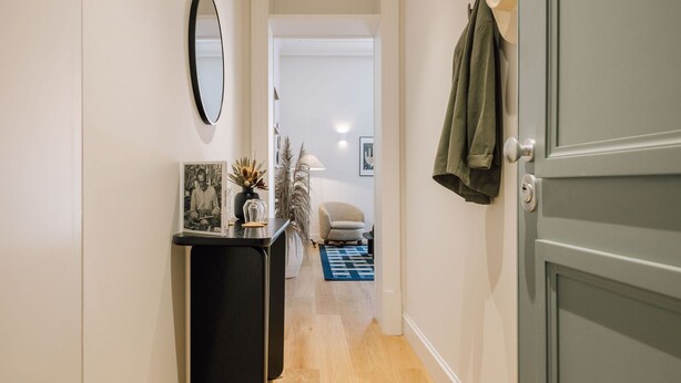 A hallway with a mirror, a small table with a vase and a framed picture, a chair, and a coat hanging on the wall. - Ando Living - Abrantes 50 House - 503 (Lisbon)