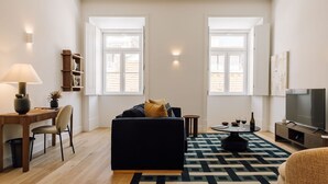 Ein modernes Wohnzimmer mit einem dunklen Sofa, einem Couchtisch, einem Fernseher und einem Bücherregal.