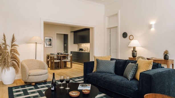 Ein modernes Wohnzimmer mit einem dunkelblauen Sofa, einem runden Couchtisch und einem Essbereich mit Holztisch und Stühlen.