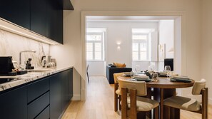 Et moderne køkken med mørke skabe, en marmor bordplade og et spiseområde med et træbord og stole.