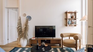 A living room with a TV, a bookshelf, a large potted plant, and a wicker chair. - Ando Living - Abrantes 50 House - 305 (Lisbon)