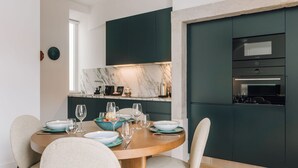 A modern kitchen with dark cabinetry, a marble backsplash, and a dining area with a round table set for six. - Ando Living - Abrantes 50 House - 506 (Lisbon)
