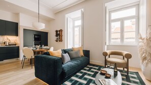 Una sala de estar moderna con un sofá verde oscuro, un comedor con mesa de madera y ventanas amplias que dejan entrar luz natural.