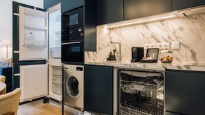 A compact kitchen with a built-in washer and dryer, a coffee machine, and a marble backsplash. - Ando Living - Abrantes 50 House - 402 (Lisbon)
