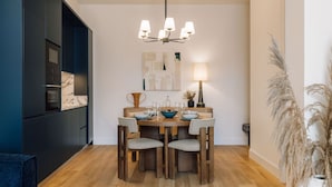 A dining area with a wooden table, four chairs, a chandelier, and a wall-mounted lamp. - Ando Living - Abrantes 50 House - 402 (Lisbon)