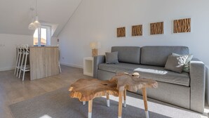 Una sala de estar moderna con un sofá gris, una mesa de centro de madera y un comedor con sillas blancas.