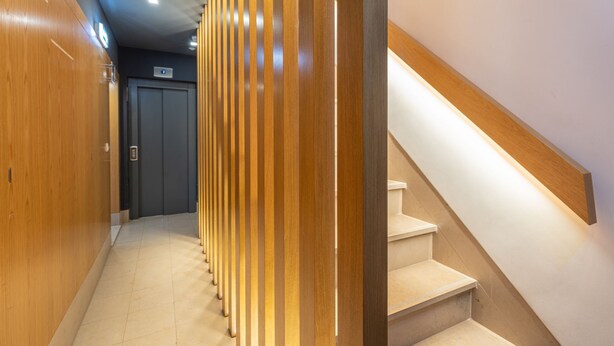 A hallway with wooden paneling, a staircase with a wooden handrail, and a door with a sign above it. - Garcia 28 Apartment 1A (Lisbon)