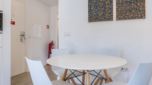 A white round table with four chairs, a fire extinguisher, and two framed artworks on the wall. - Garcia 28 Apartment 1A (Lisbon)