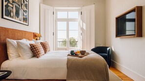 A hotel room with a large bed, a TV mounted on the wall, and a balcony with a view. - Ando Living - Corpo Santo House - 401 (Lisbon)