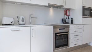 A modern kitchen with white cabinets, a Bosch oven, a Bosch microwave, a coffee maker, and a sink. - Garcia 28 Apartment 3A (Lisbon)