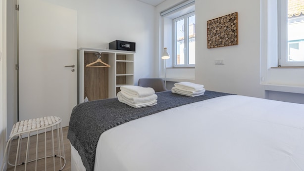 A neatly arranged bedroom with a bed, a bedside table, a hanging wardrobe, and a window with a view. - Garcia 28 Apartment 3A (Lisbon)
