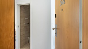 A hotel room entrance with a wooden door, a white wall, and a tiled shower area. - Garcia 28 Apartment 3A (Lisbon)