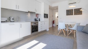 A modern kitchen with white cabinets, a built-in oven, and a microwave. There is a dining area with a table and chairs, and a gray rug on the floor. - Garcia 28 Apartment 3A (Lisbon)