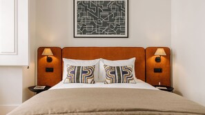 A hotel room with a bed, two bedside lamps, a nightstand, a framed abstract artwork, and a beige throw blanket. - Ando Living - Corpo Santo House - 301 (Lisbon)